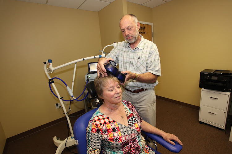 Clinician administering transcranial magnetic stimulation treatment to patient in yellow clinic room