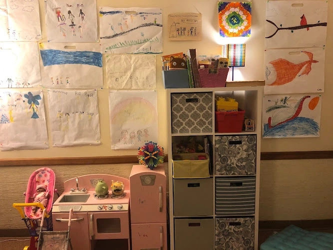 Children's therapy room with colorful artwork on walls, toy kitchen, storage cubbies, and developmental toys