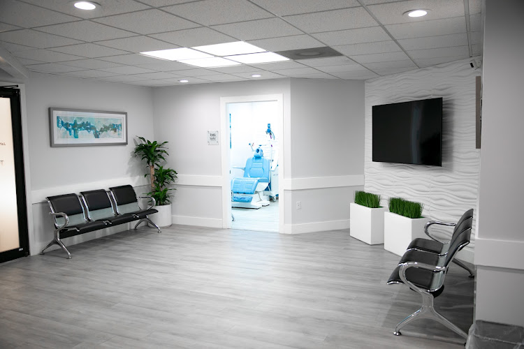 TMS of Miami waiting room with black seating, potted plants, wall-mounted TV, and treatment room visible through doorway