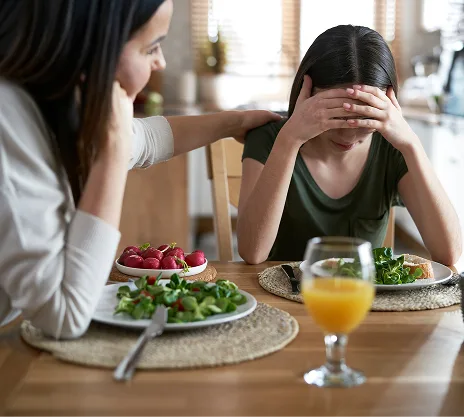 Woman offering support to another woman at dinner table with healthy food and juice