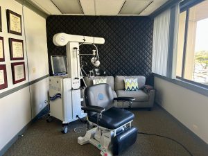 TMS treatment room with patient chair, robotic arm device, monitor, and sofa against quilted accent wall