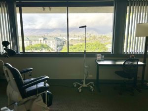 Consultation room with patient chair, desk, and large windows overlooking mountain and residential landscape