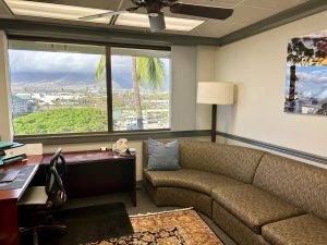 Office interior with desk, seating area, and panoramic windows framing mountains and palm trees