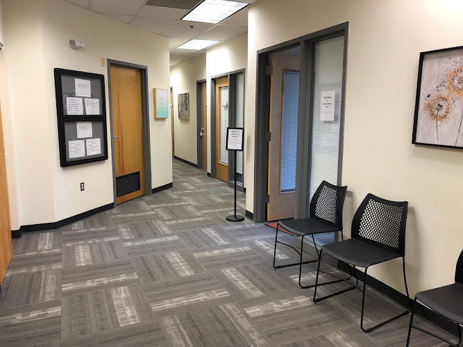 Clinic hallway with treatment room doors, black chairs, and information boards