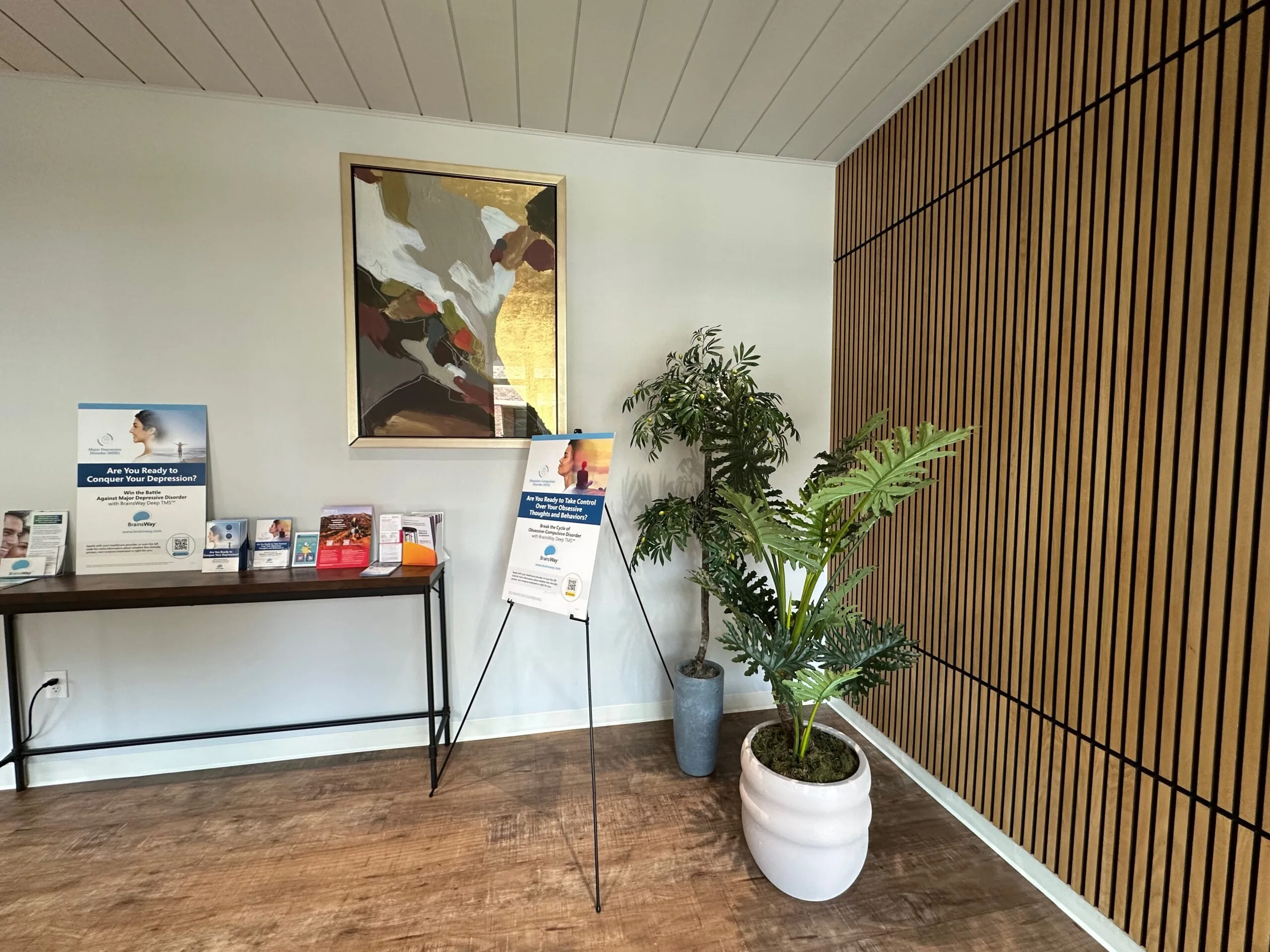 TMS clinic waiting area with promotional materials on shelf, potted plants, and wooden accent wall
