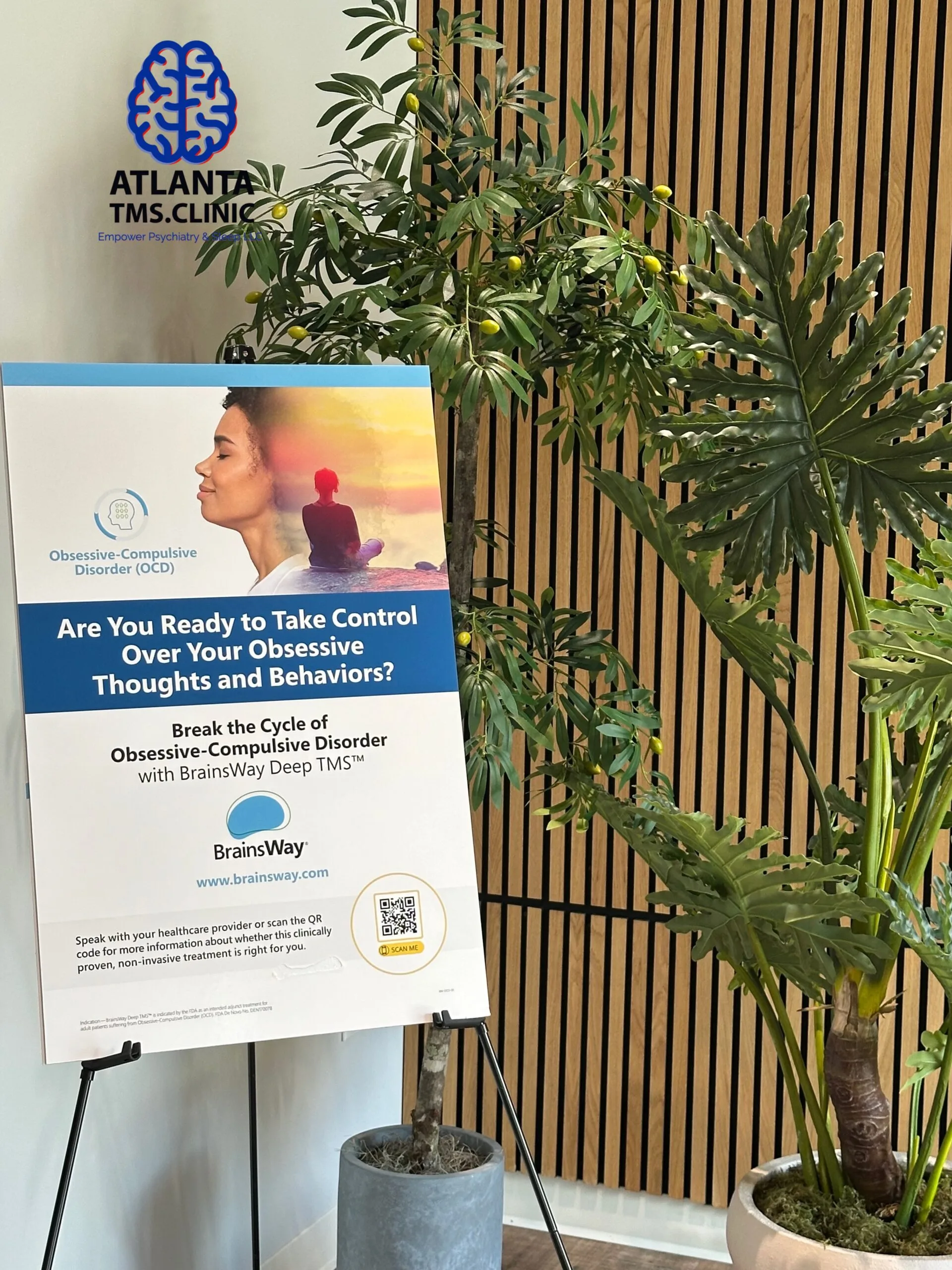 Atlanta TMS.Clinic logo above informational sign about obsessive-compulsive disorder treatment with potted plant