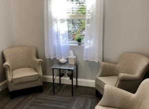 Serene waiting area with two beige armchairs flanking a small table by a window with sheer curtains