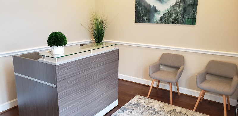 Woodlands Psychiatry Group reception area with modern desk, potted plants, landscape artwork, and gray upholstered chairs