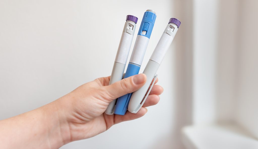 Hand holding three injectable pens with purple and blue caps