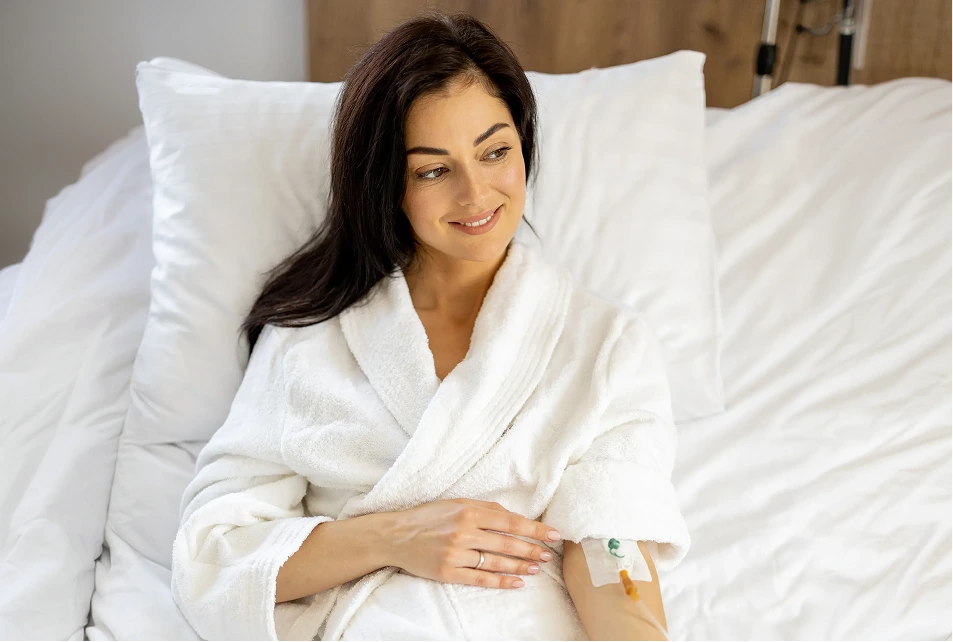 Woman in white robe relaxing on bed during IV drip therapy session