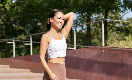 Fit woman in athletic wear posing outdoors with trees and sports court in background