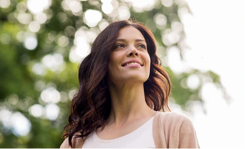 Woman smiling outdoors with natural bokeh background