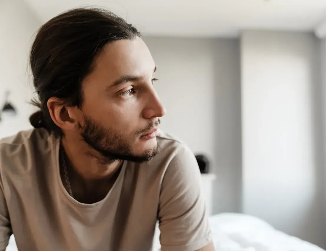 Man sitting on bed at night, gazing toward window with troubled expression