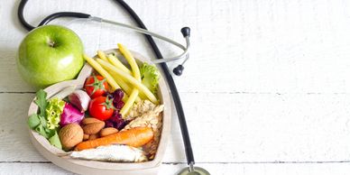 Stethoscope with healthy food including apple, vegetables, and grains on white surface
