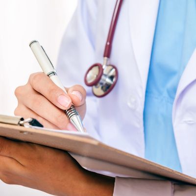 Healthcare provider holding pen and clipboard wearing white coat with stethoscope