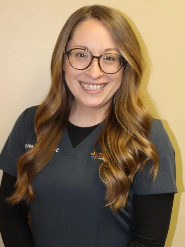 Staff member wearing glasses and dark scrubs with Tristan Medical logo smiling at camera