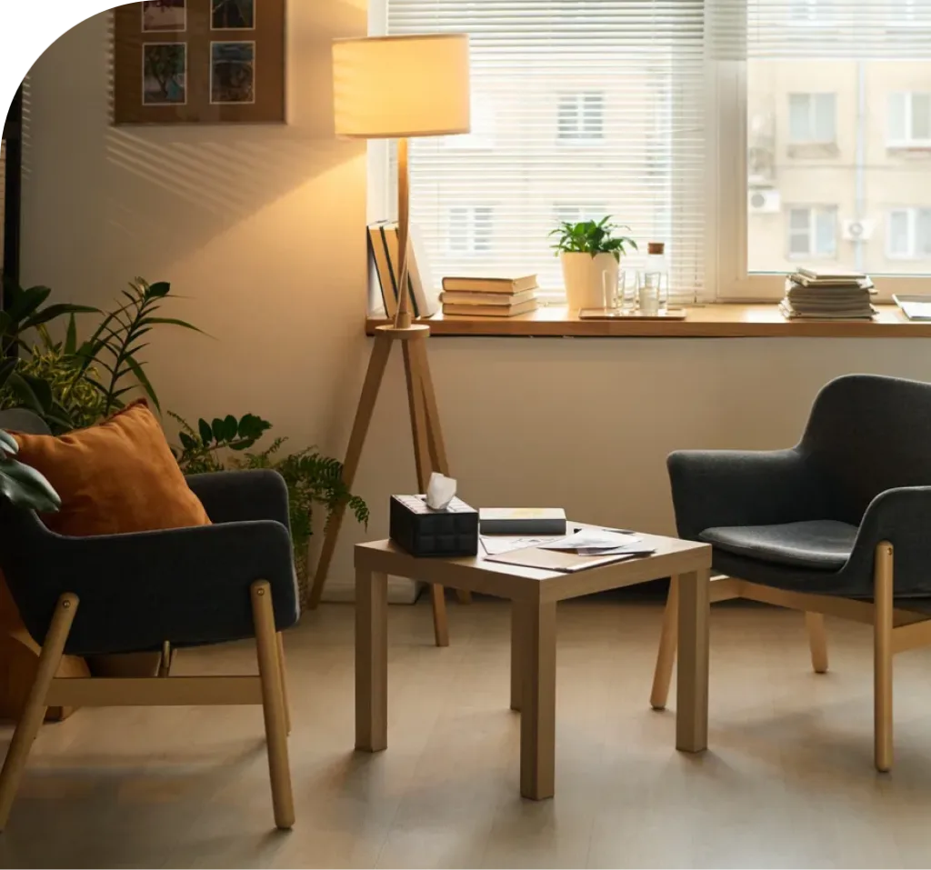 Warm therapy office with two armchairs, lamp, plants, and window seating area