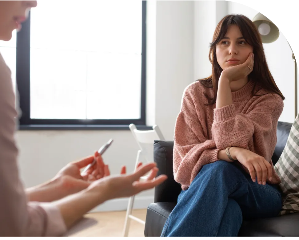 Mental health professional taking notes while speaking with woman in pink sweater during consultation