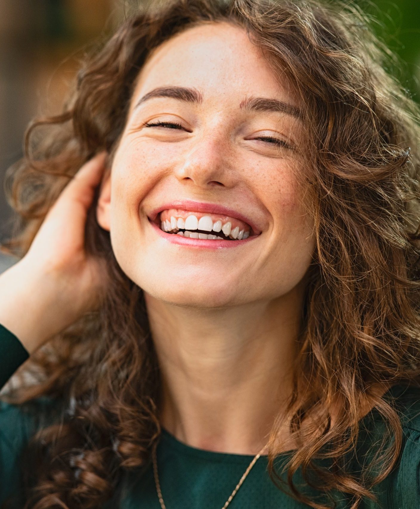 Woman with wavy hair smiling with hand near face
