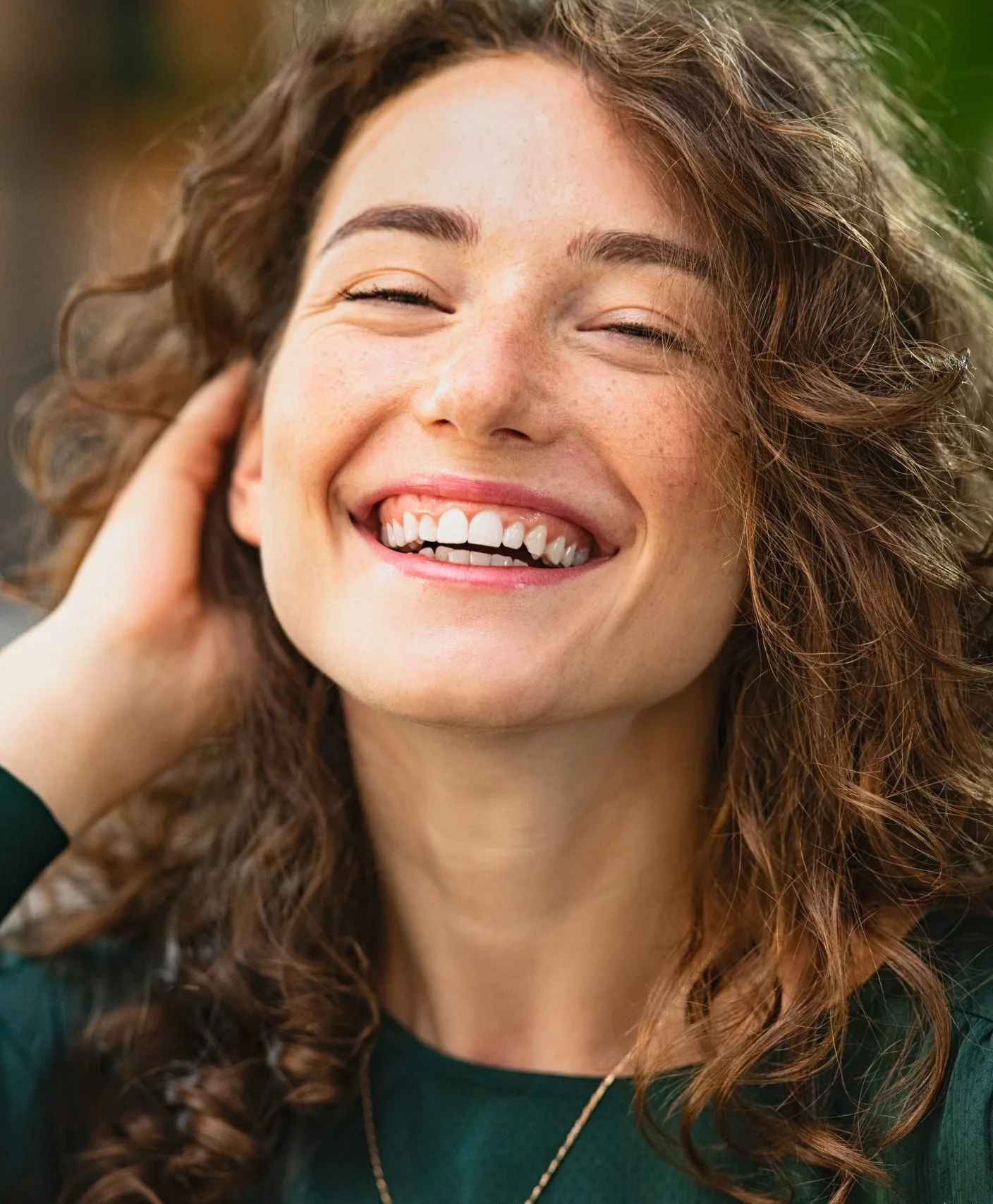 Woman with wavy hair smiling with hand near face