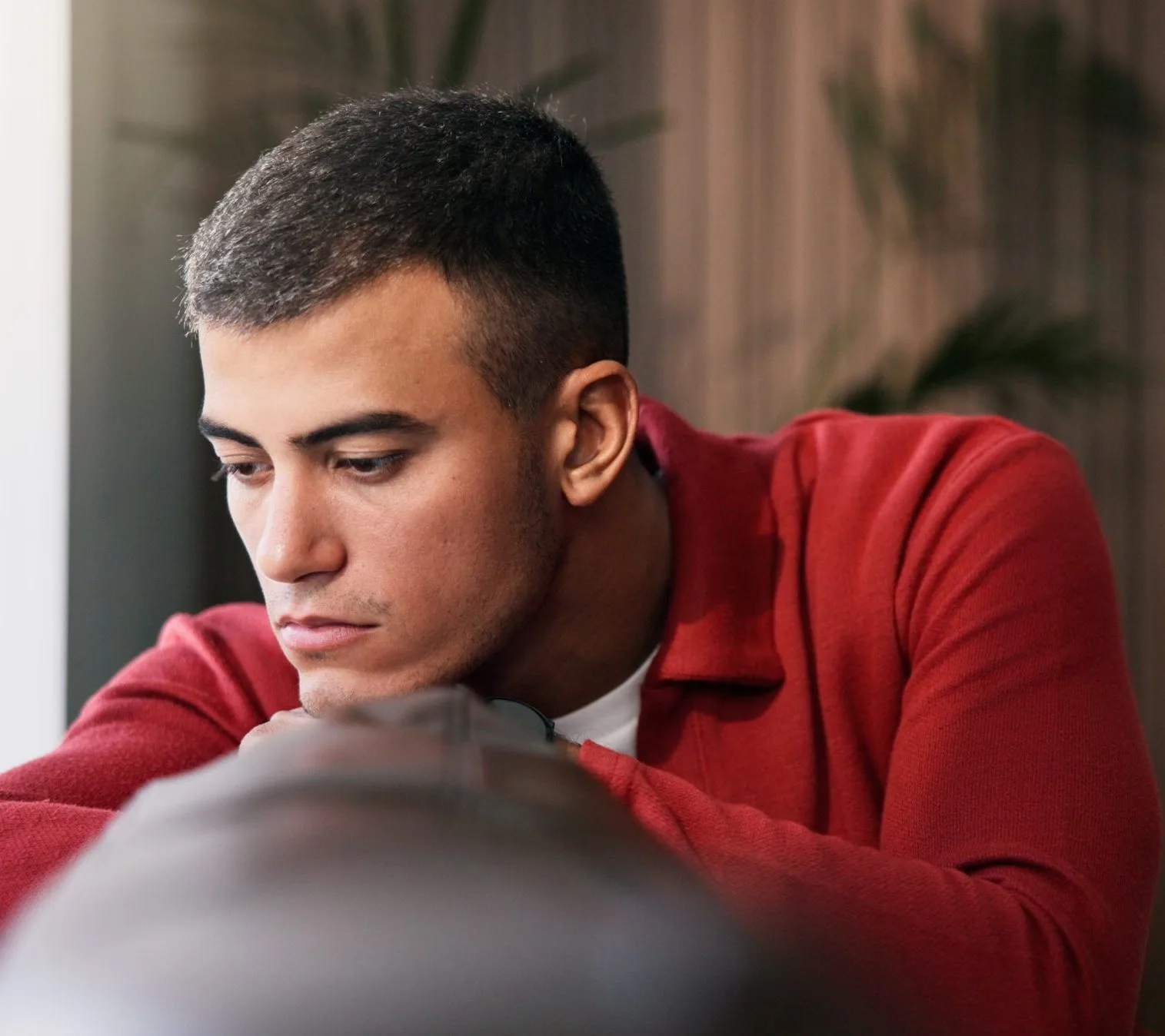Man in red shirt looking down pensively, with blurred indoor background