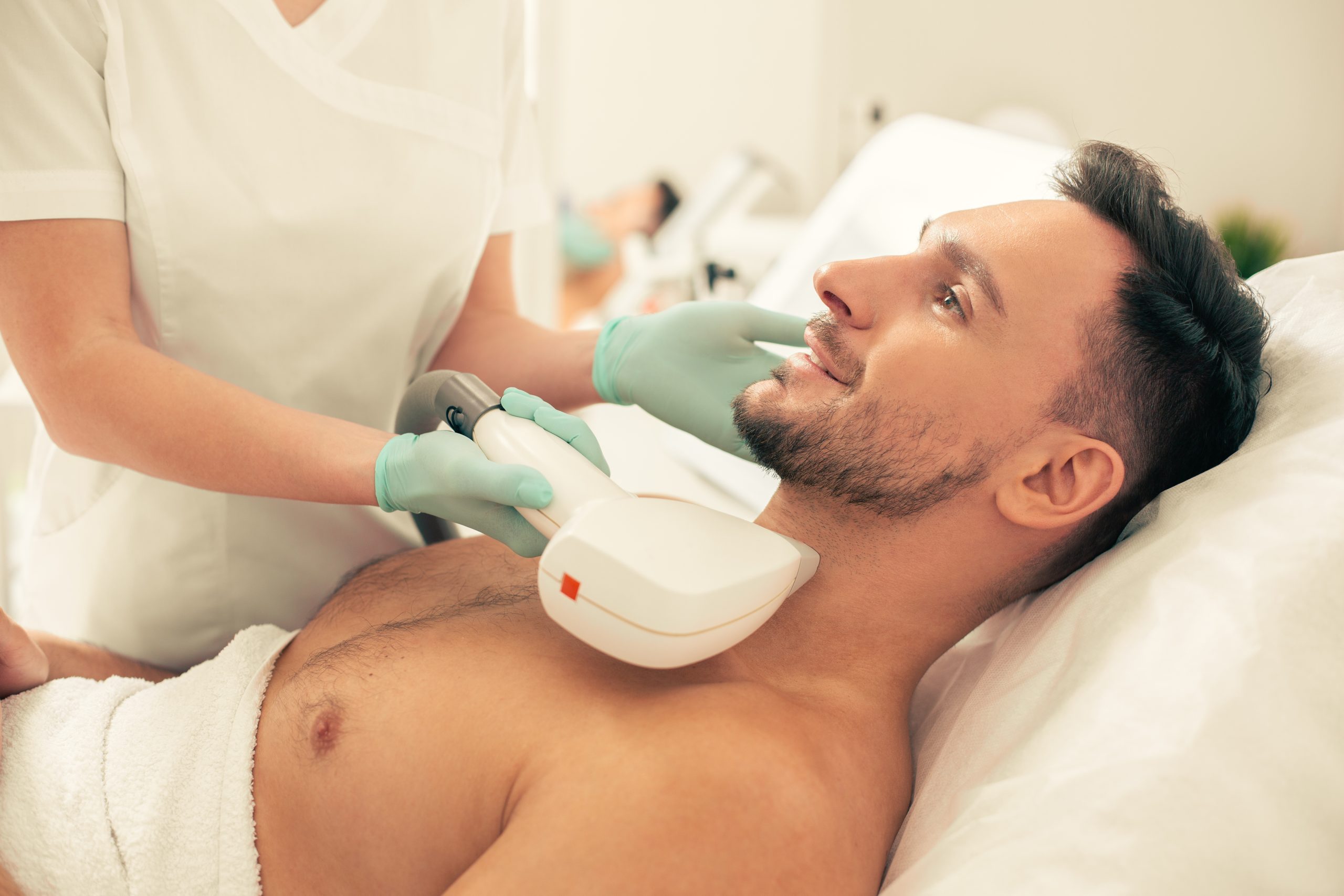 Technician performing laser hair removal on man's neck and chest area