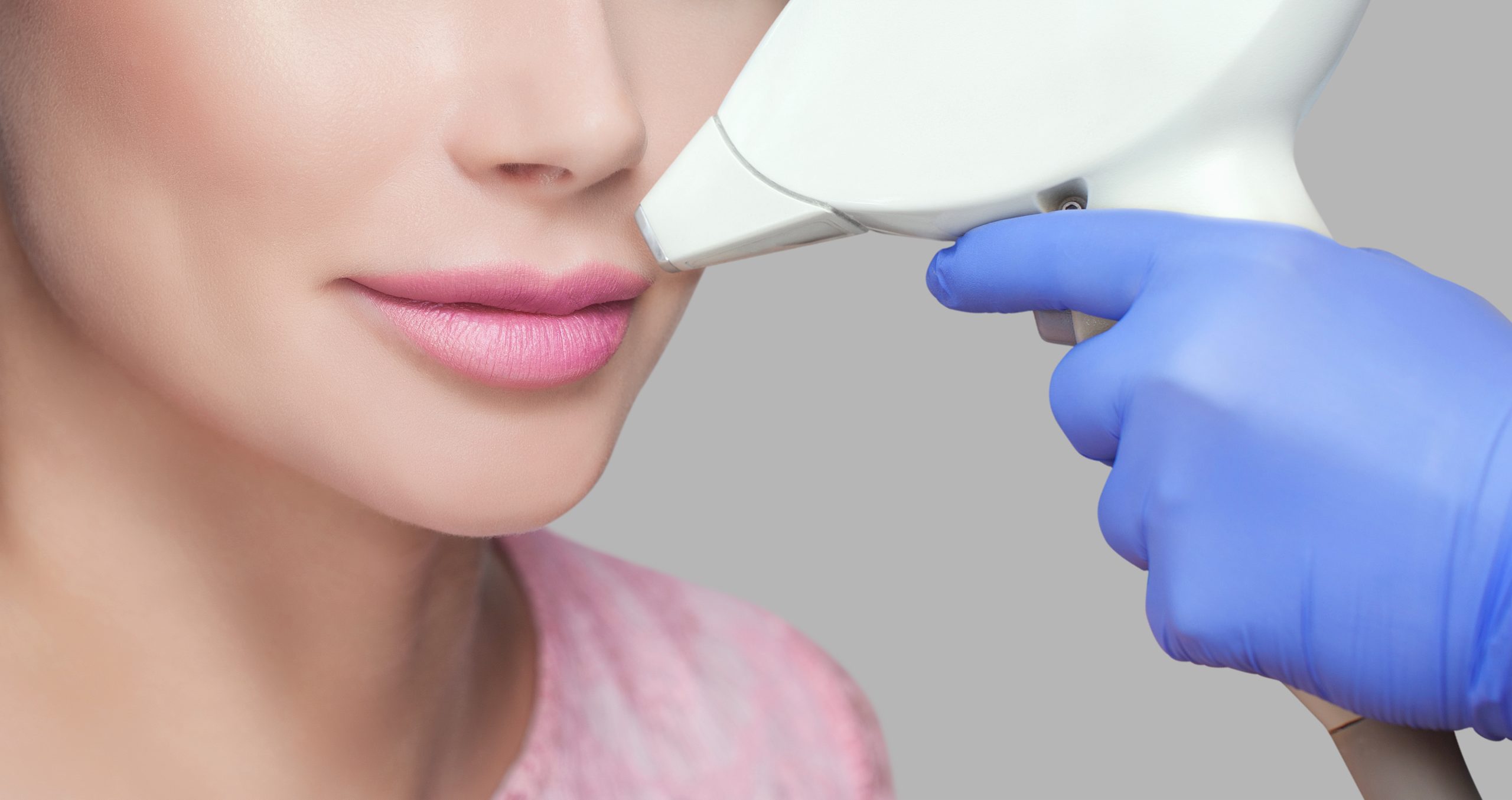 Practitioner in blue gloves using laser device on woman's upper lip area