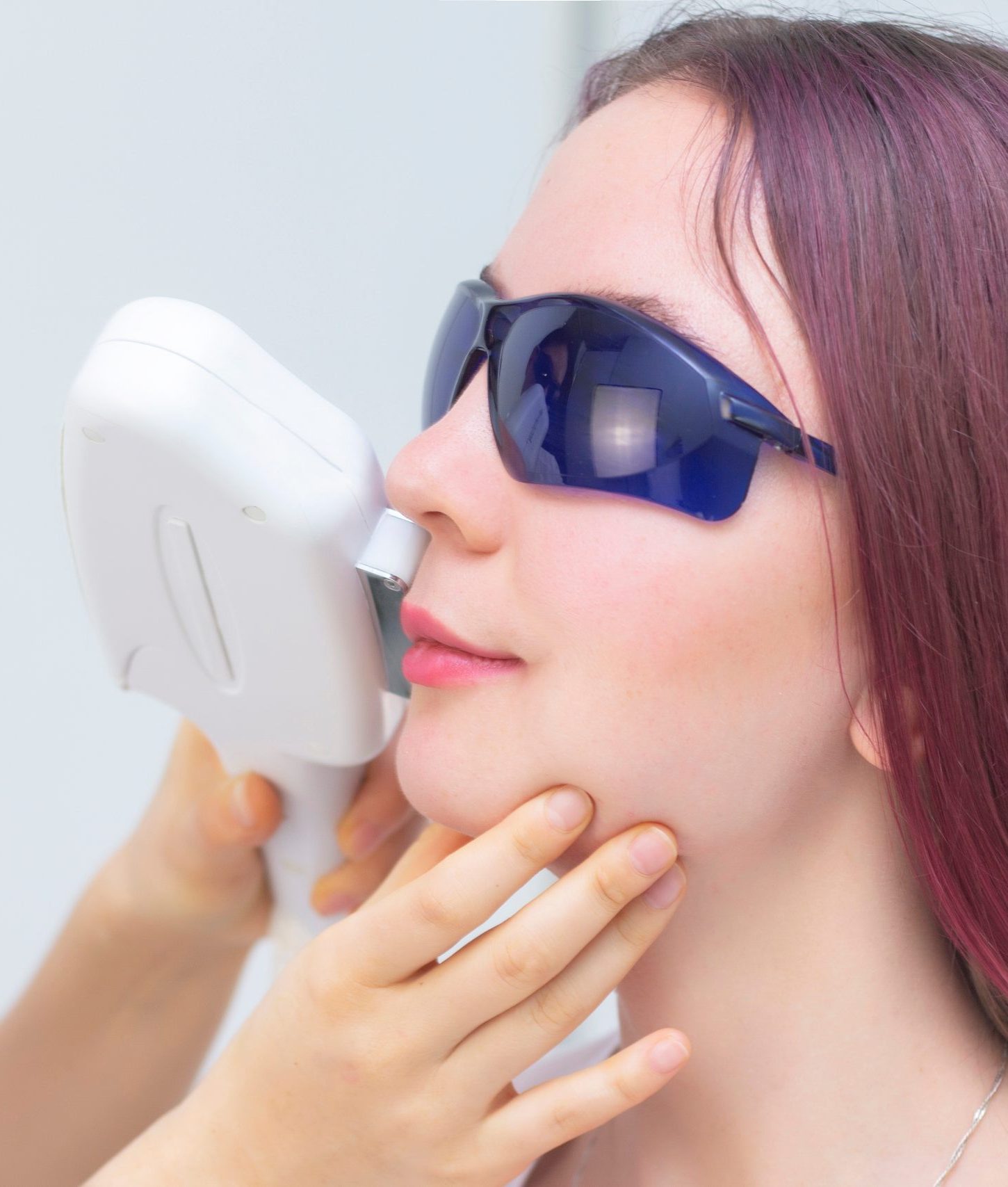 Woman wearing protective eyewear holding laser hair removal device to her face