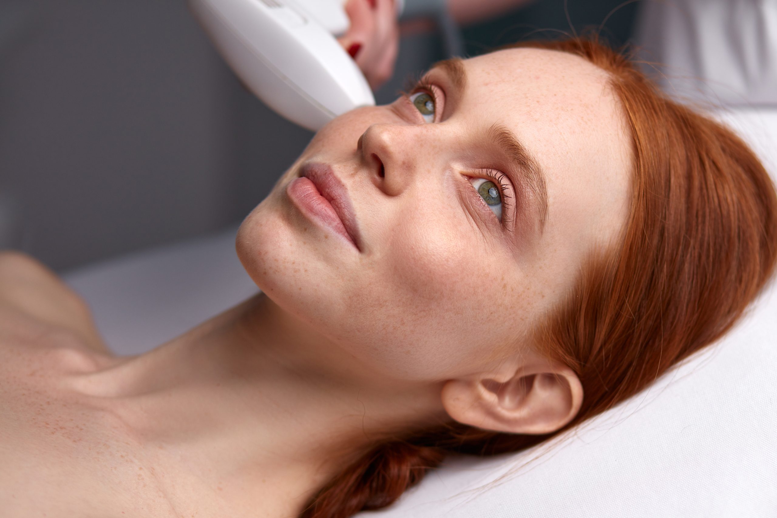 Woman receiving RF face lifting treatment with handheld device applied to her cheek