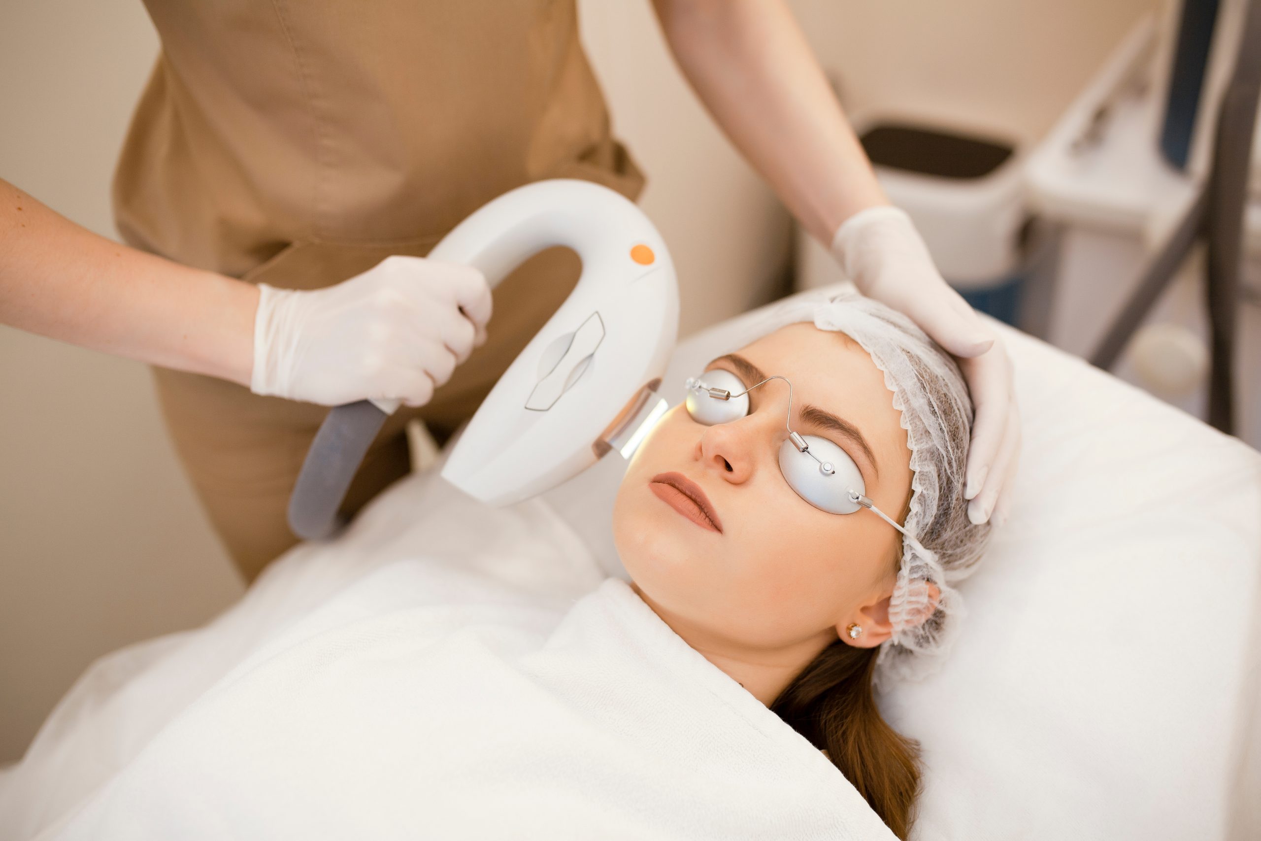 Aesthetician performing IPL treatment on woman's face wearing protective eyewear and headband