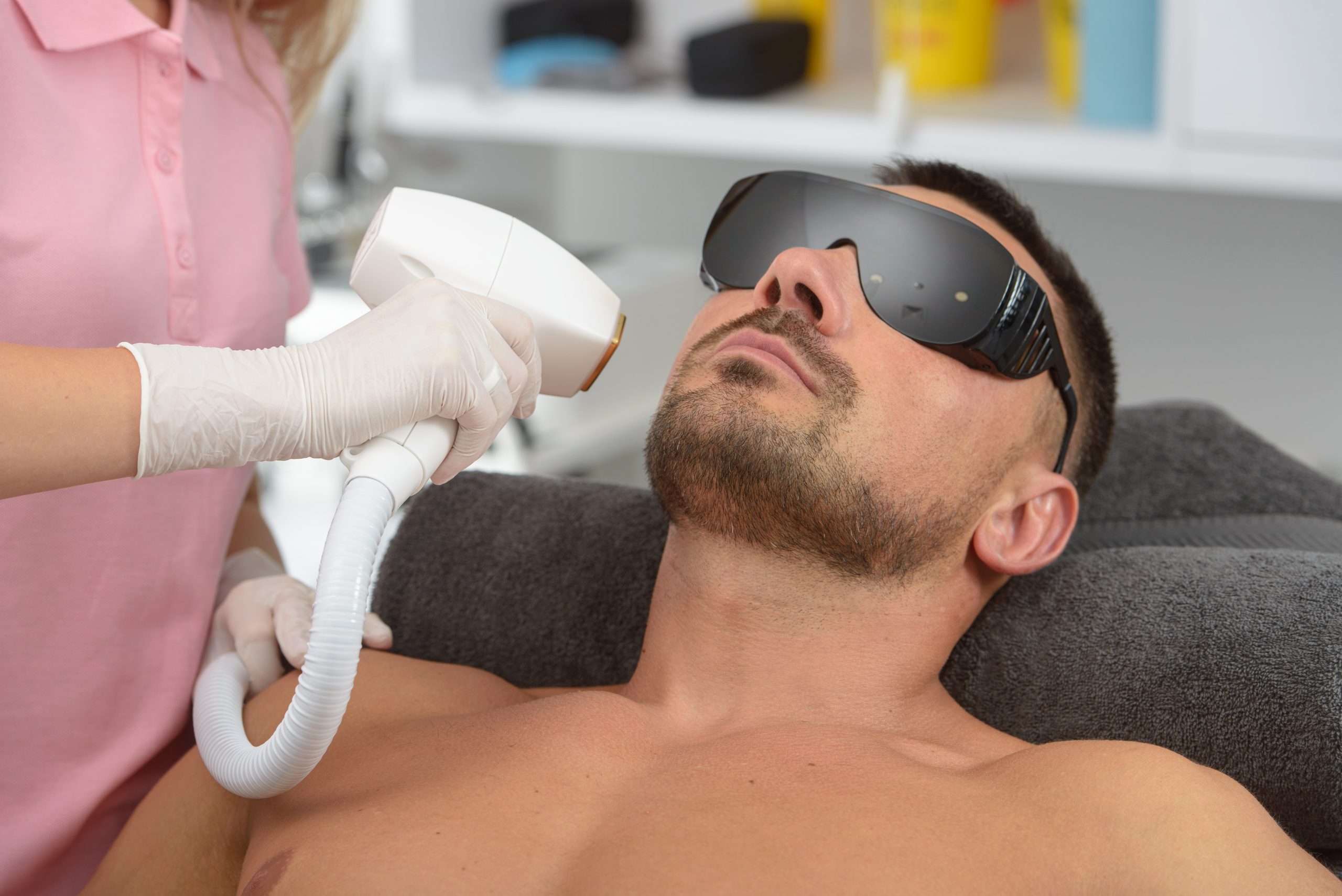Male patient wearing protective eyewear receives facial laser hair removal treatment from a provider in a clinical setting