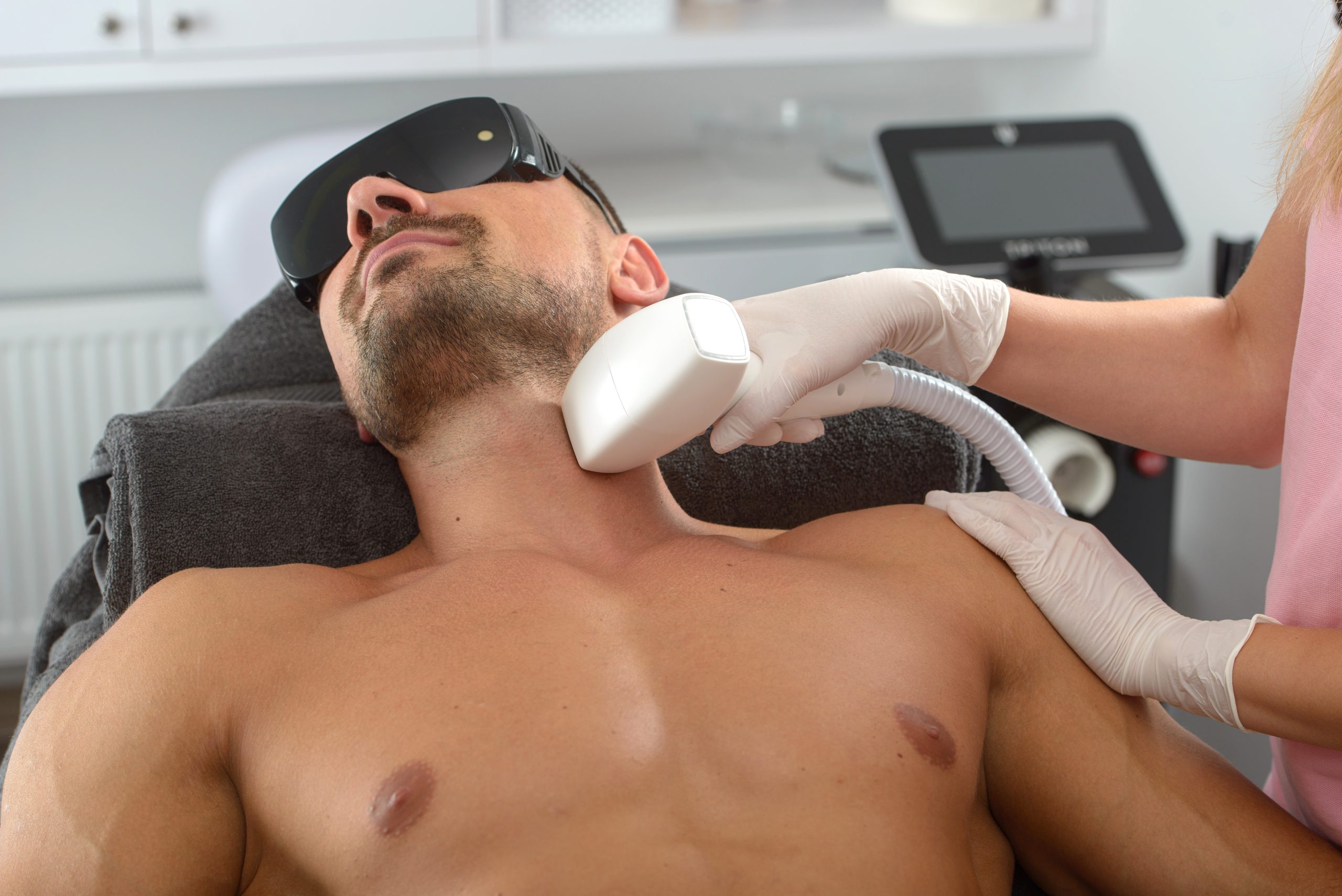Practitioner applying laser hair removal handpiece to man's neck during treatment