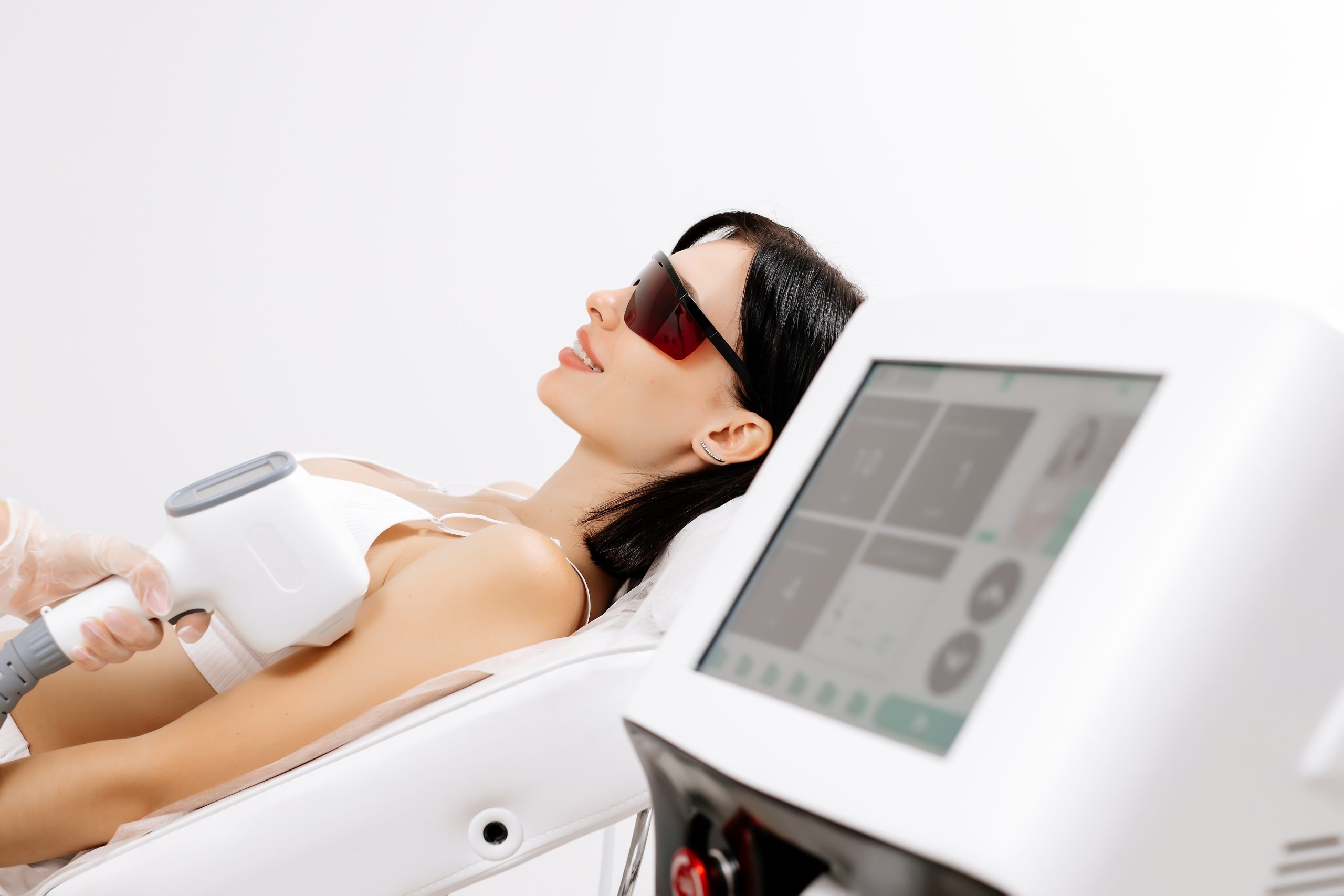 Woman wearing protective eyewear receives laser hair removal treatment on her arm from a handheld device
