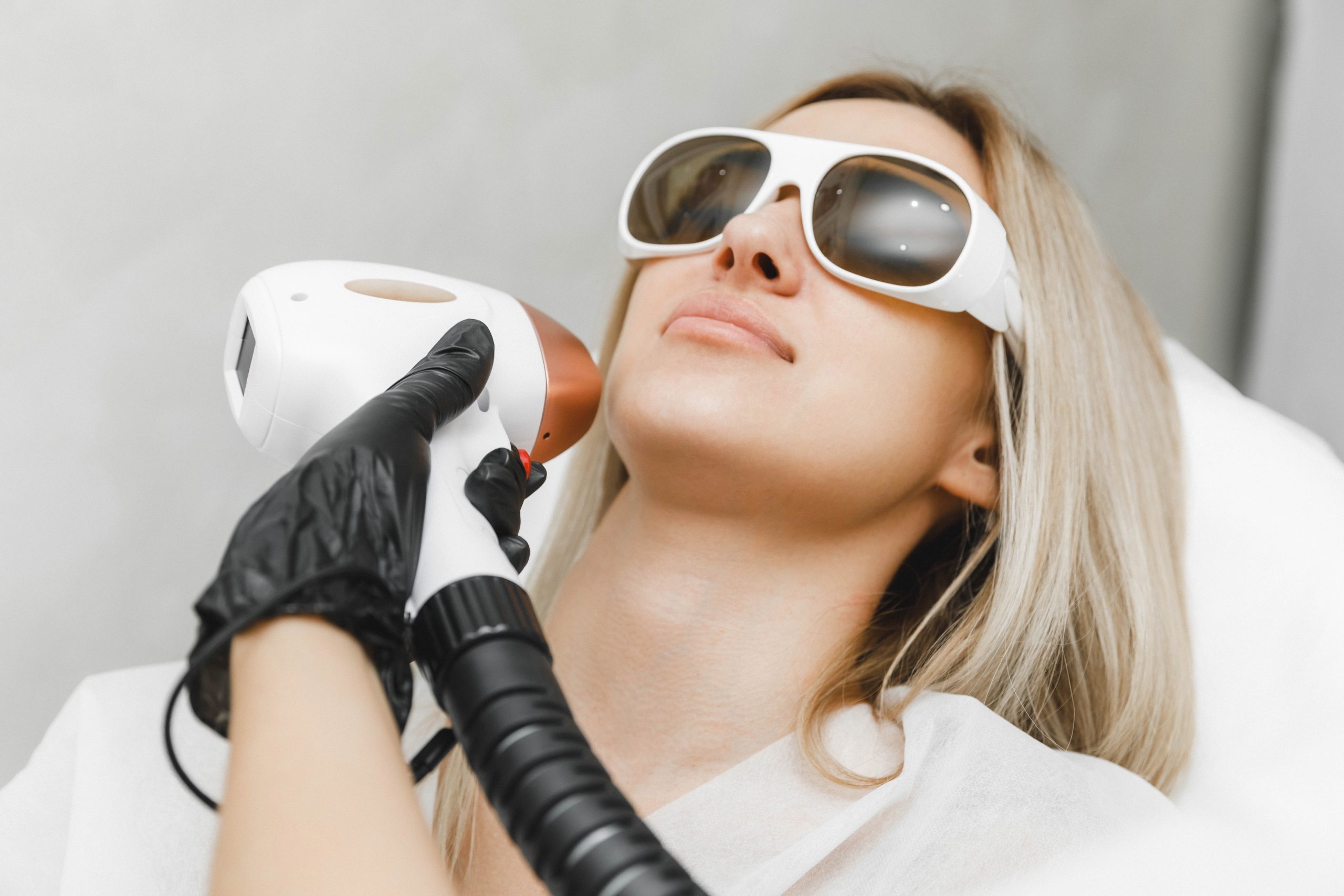 Woman wearing protective eyewear receives laser hair removal treatment to her face