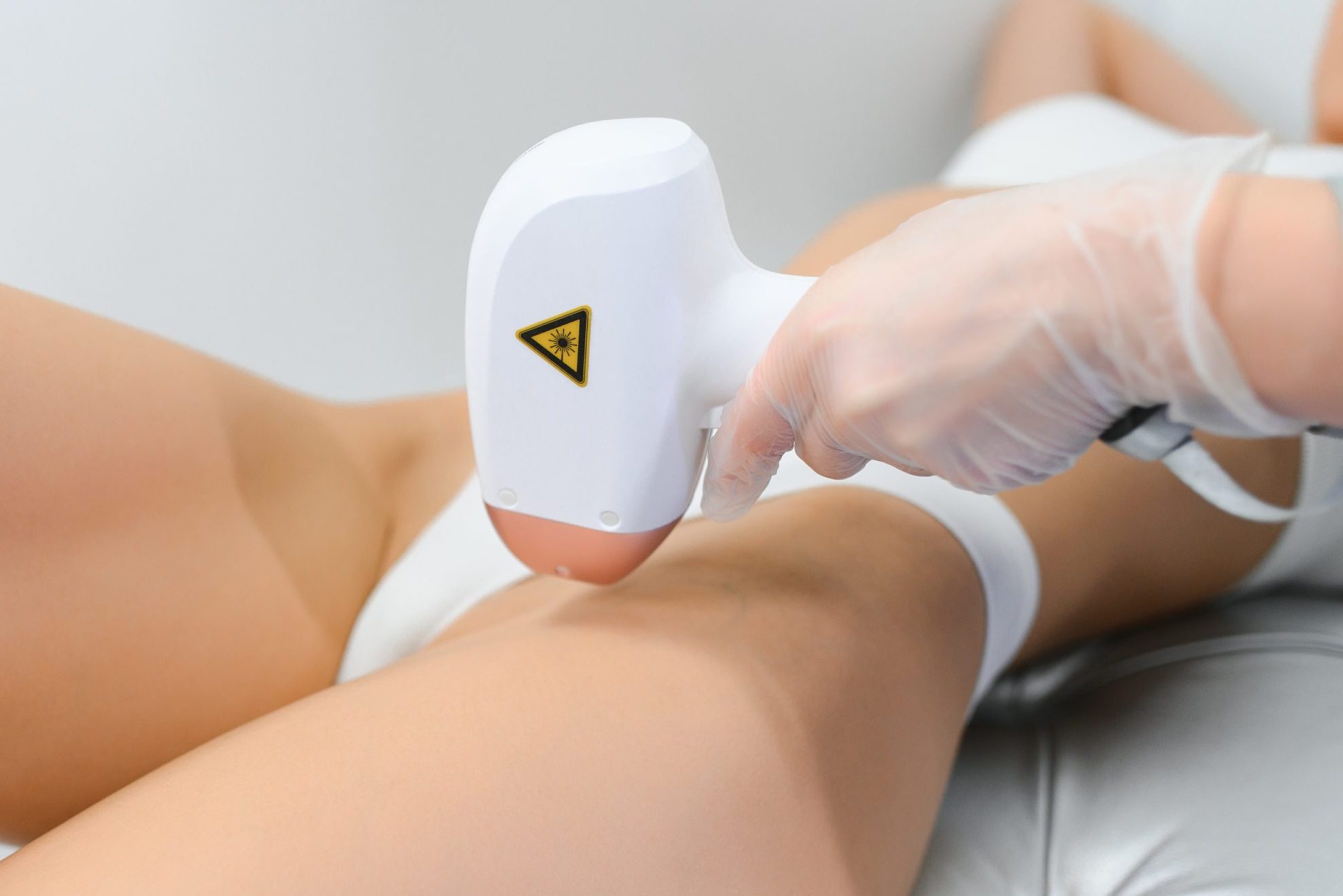 Practitioner using handheld laser hair removal device on patient's leg