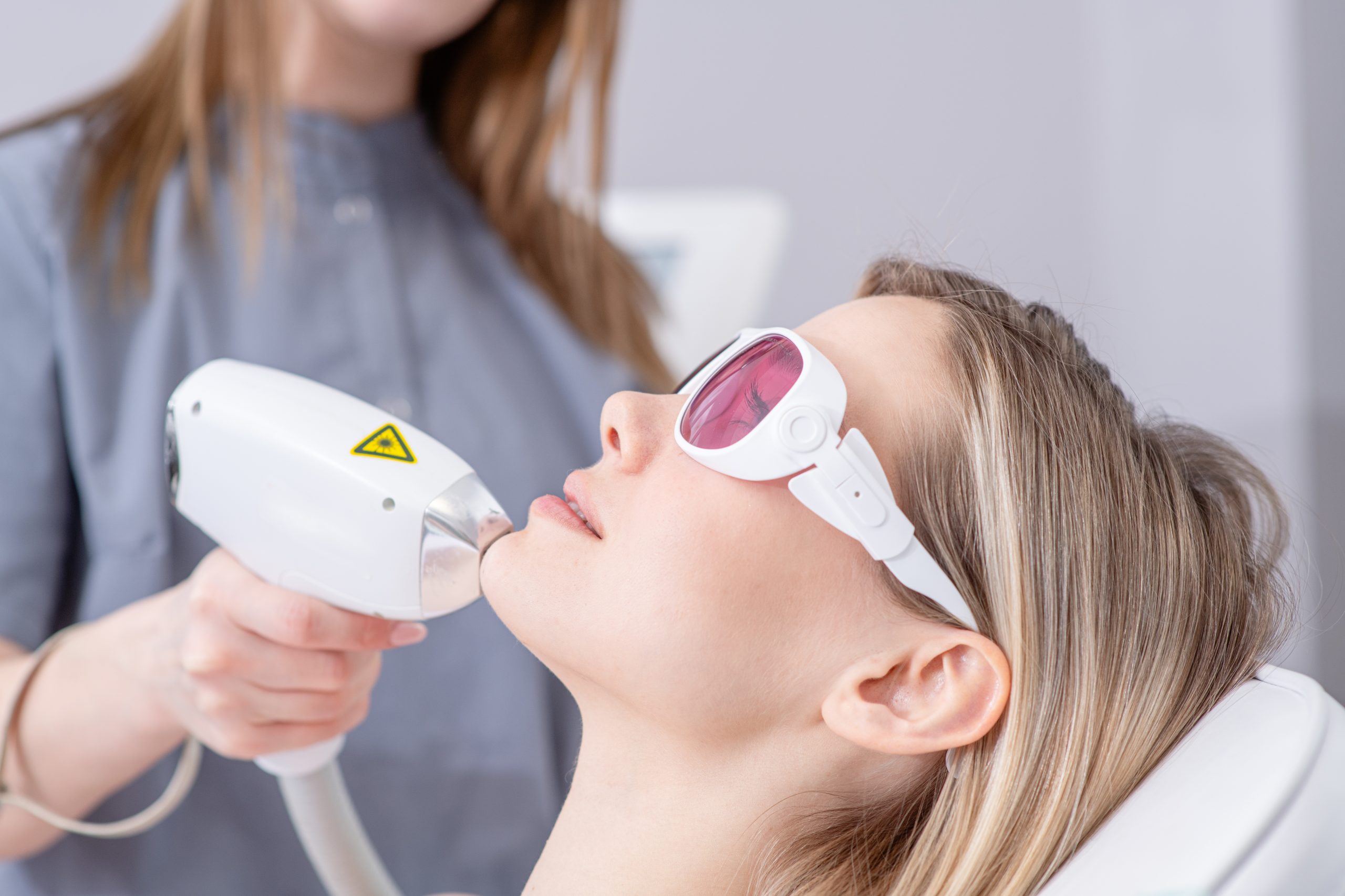 Clinician using laser hair removal device on patient's chin while patient wears protective eyewear