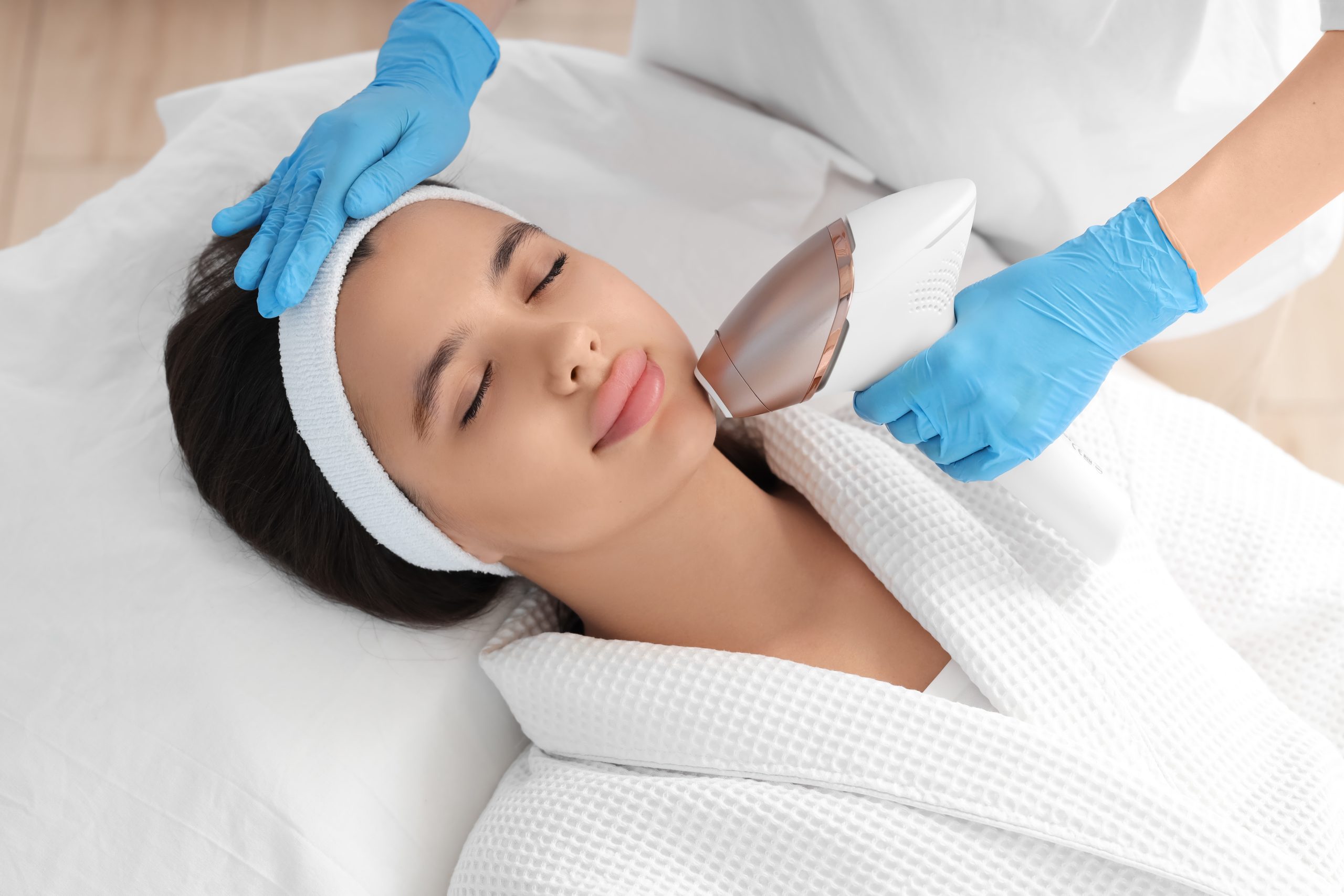 Practitioner in blue gloves performing laser hair removal treatment on patient's chin