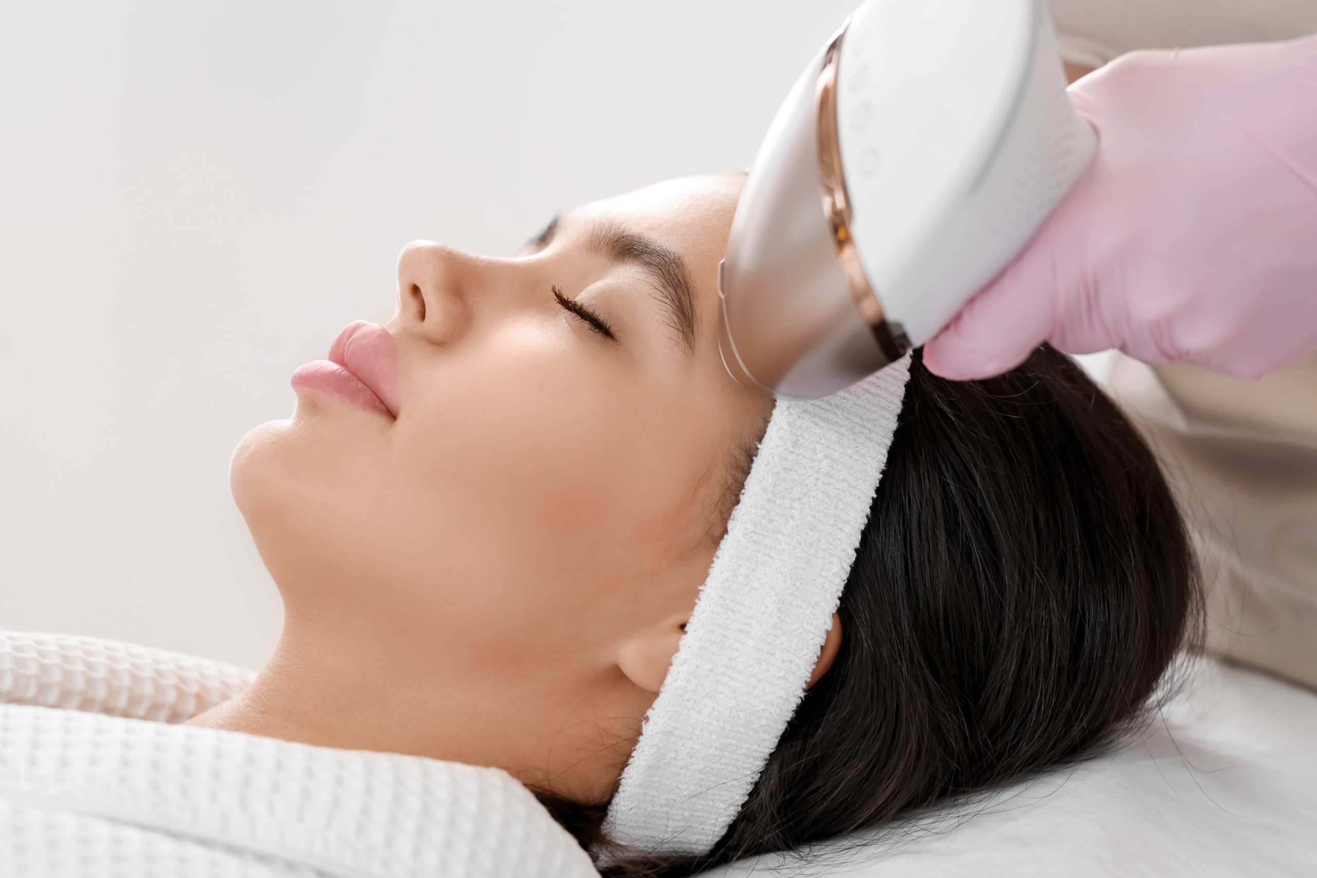 Aesthetician using a laser device on a woman's eyebrow area during hair removal treatment