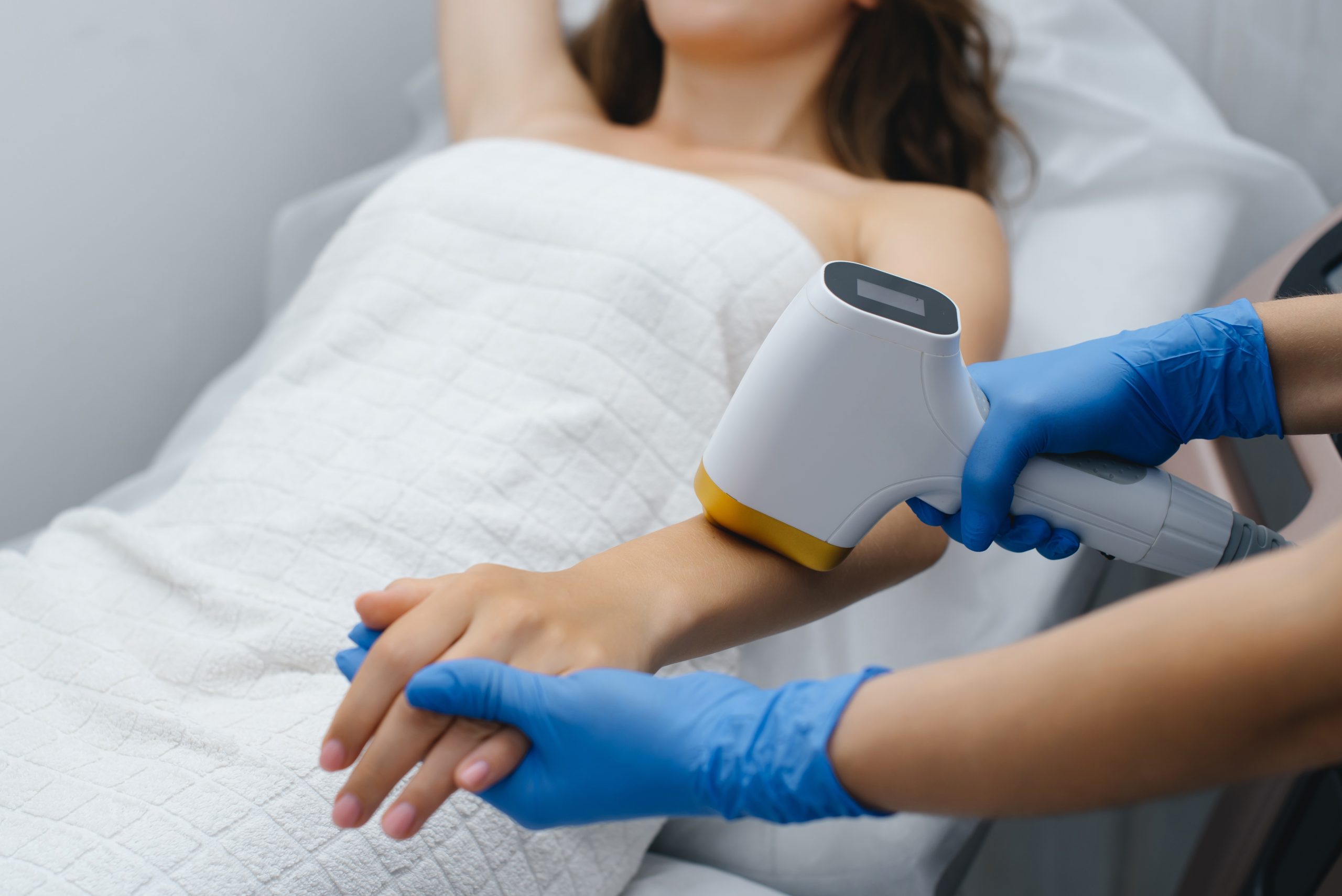 Practitioner in blue gloves applying laser hair removal device to woman's arm during treatment