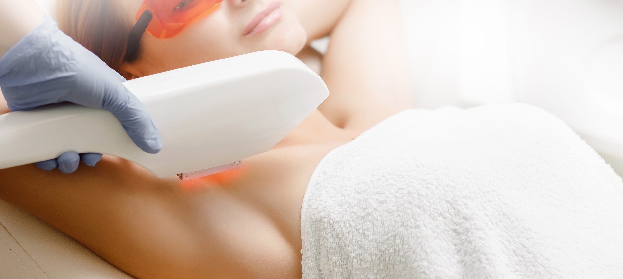 Clinician in gloves using handheld laser device on patient's underarm during hair removal treatment