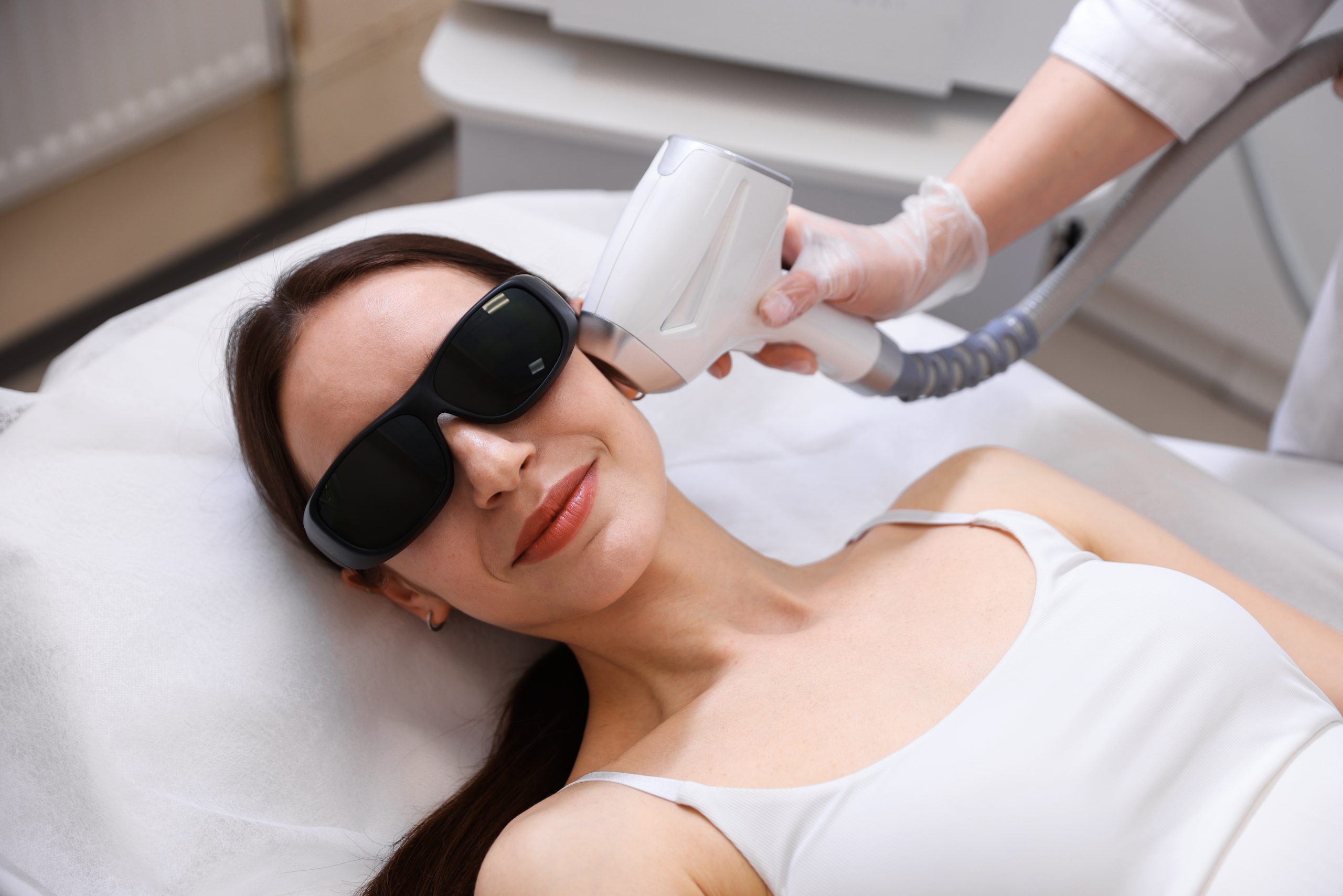 Practitioner performing laser hair removal on woman's face wearing protective eyewear