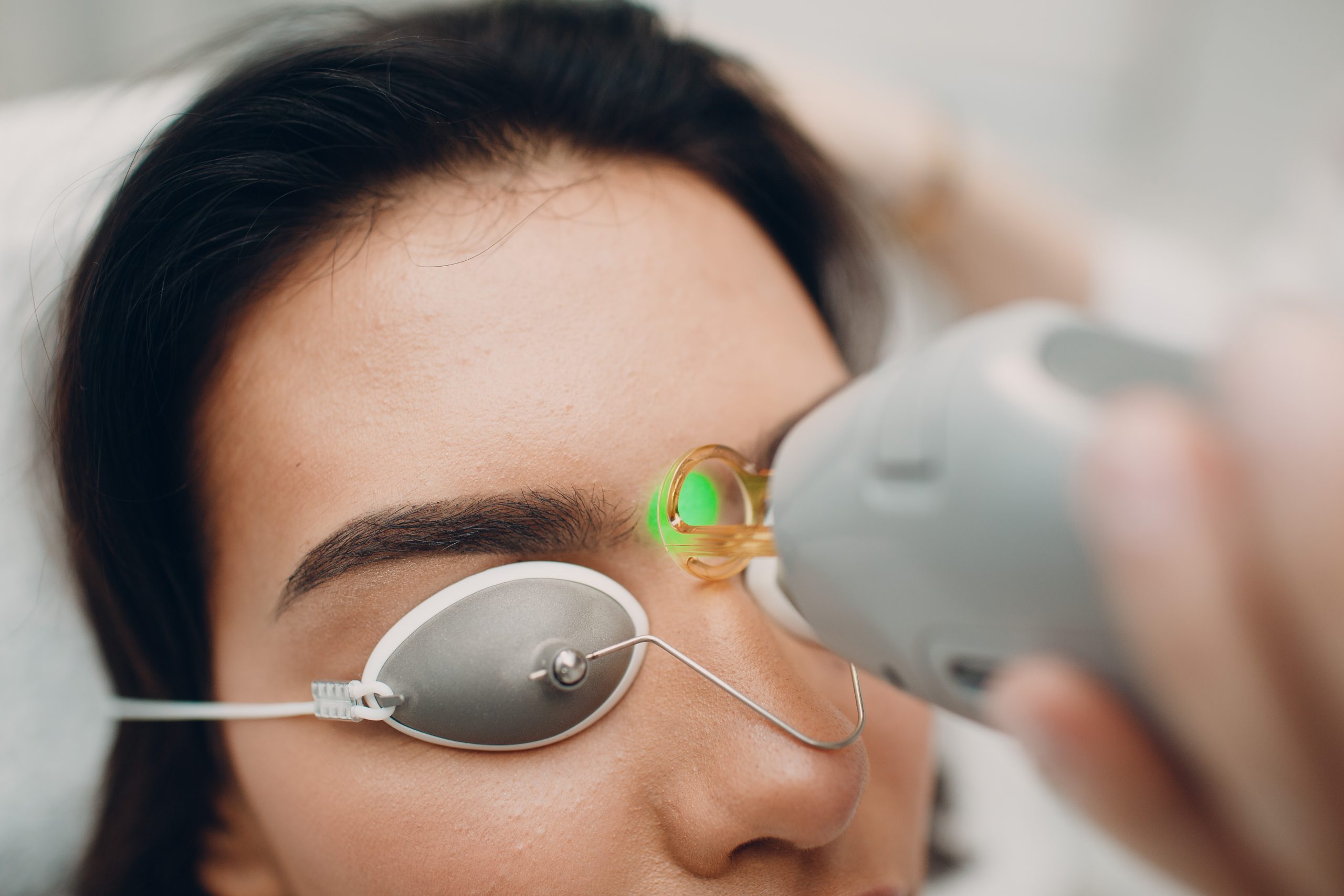 Woman wearing protective eyewear receiving laser hair removal treatment on her eyebrow