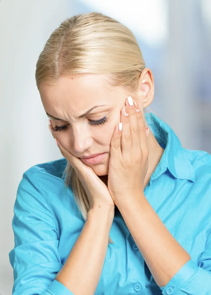 Woman in blue shirt touching jaw with hand, showing discomfort
