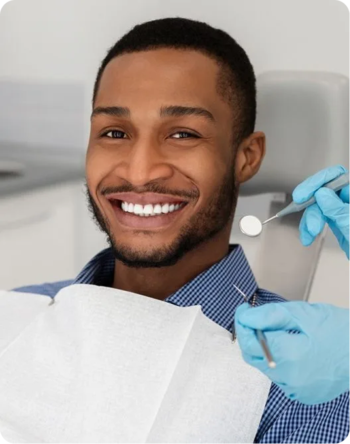 Smiling patient in dental chair with dentist holding mirror and explorer tool during examination