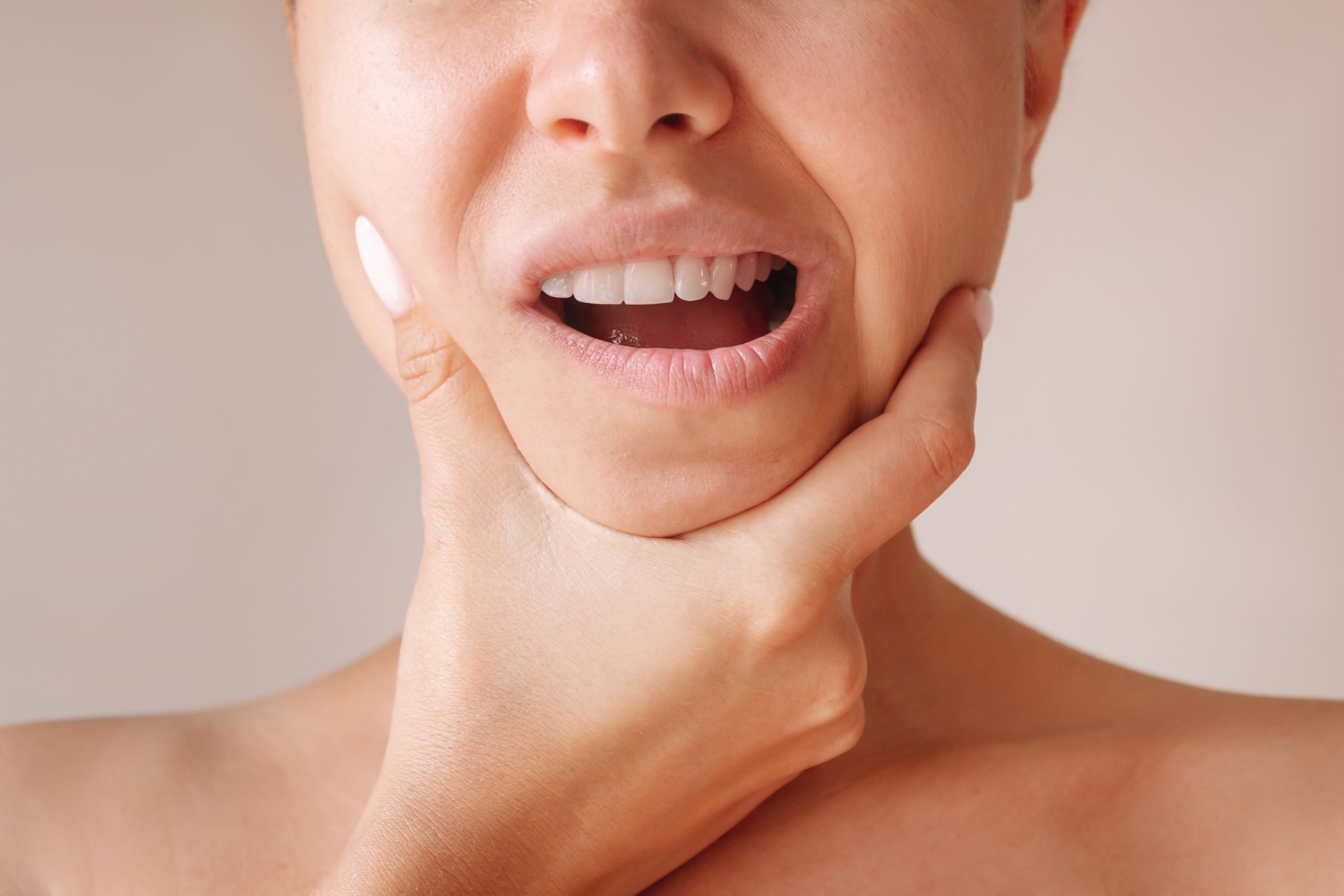 Man holding his jaw with both hands, mouth open wide, showing signs of jaw pain or lockjaw