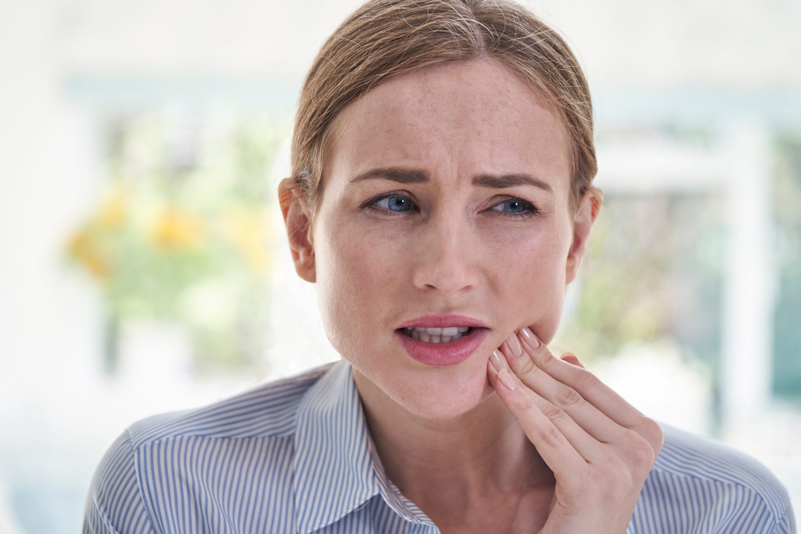 Woman touching her cheek and grimacing with expression of dental pain or discomfort