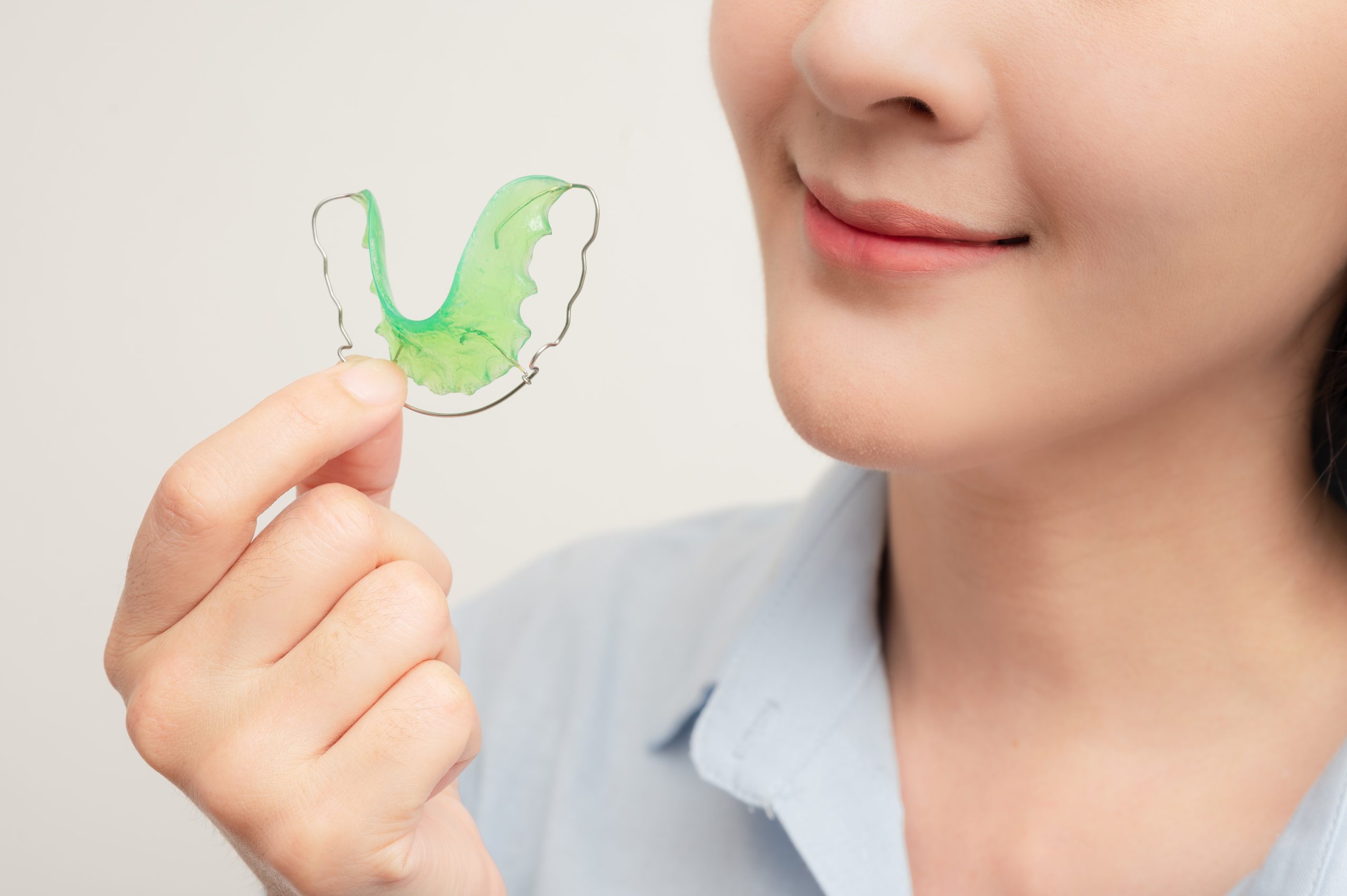 Woman holding green orthodontic retainer near her smile