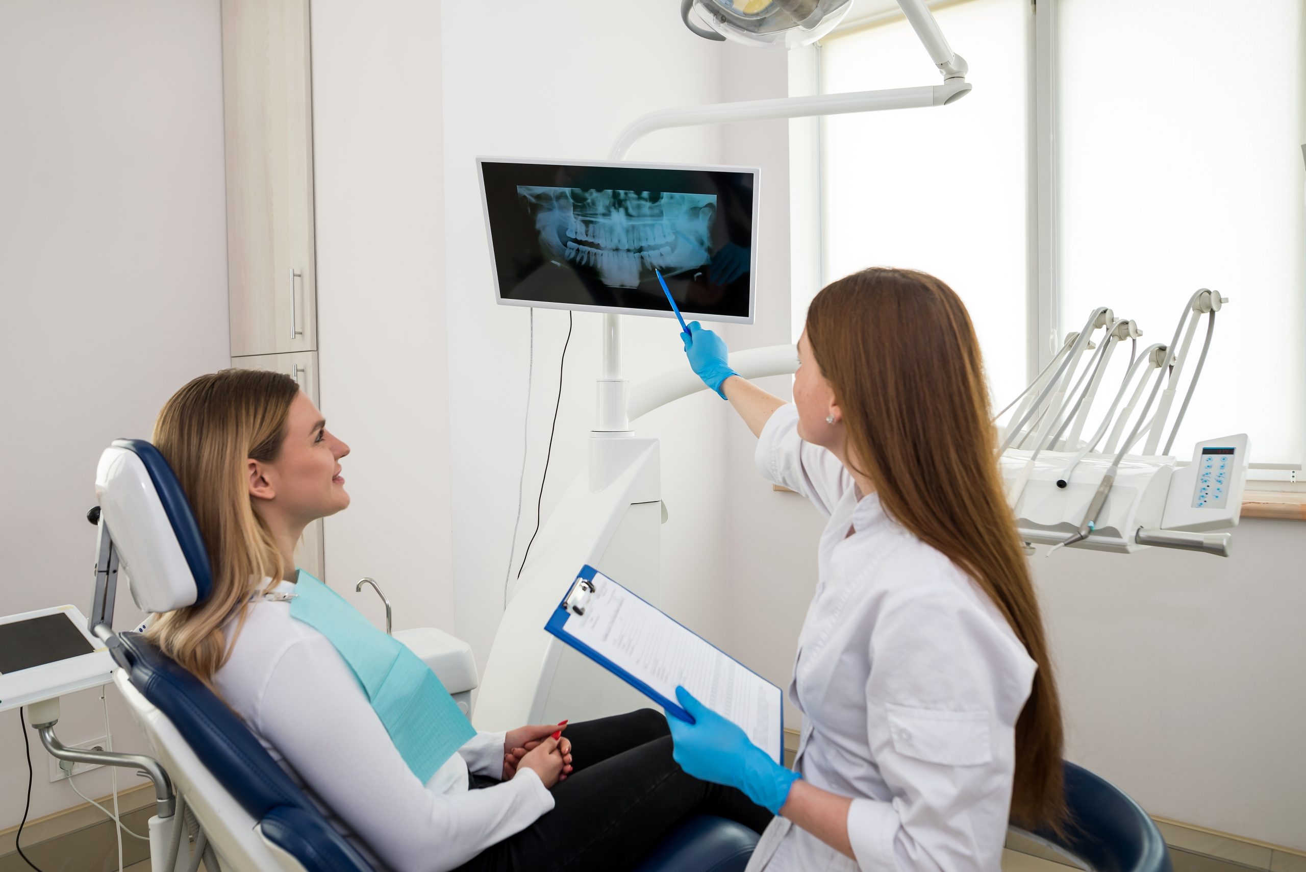 Dentist pointing to patient's dental X-ray displayed on monitor in treatment room