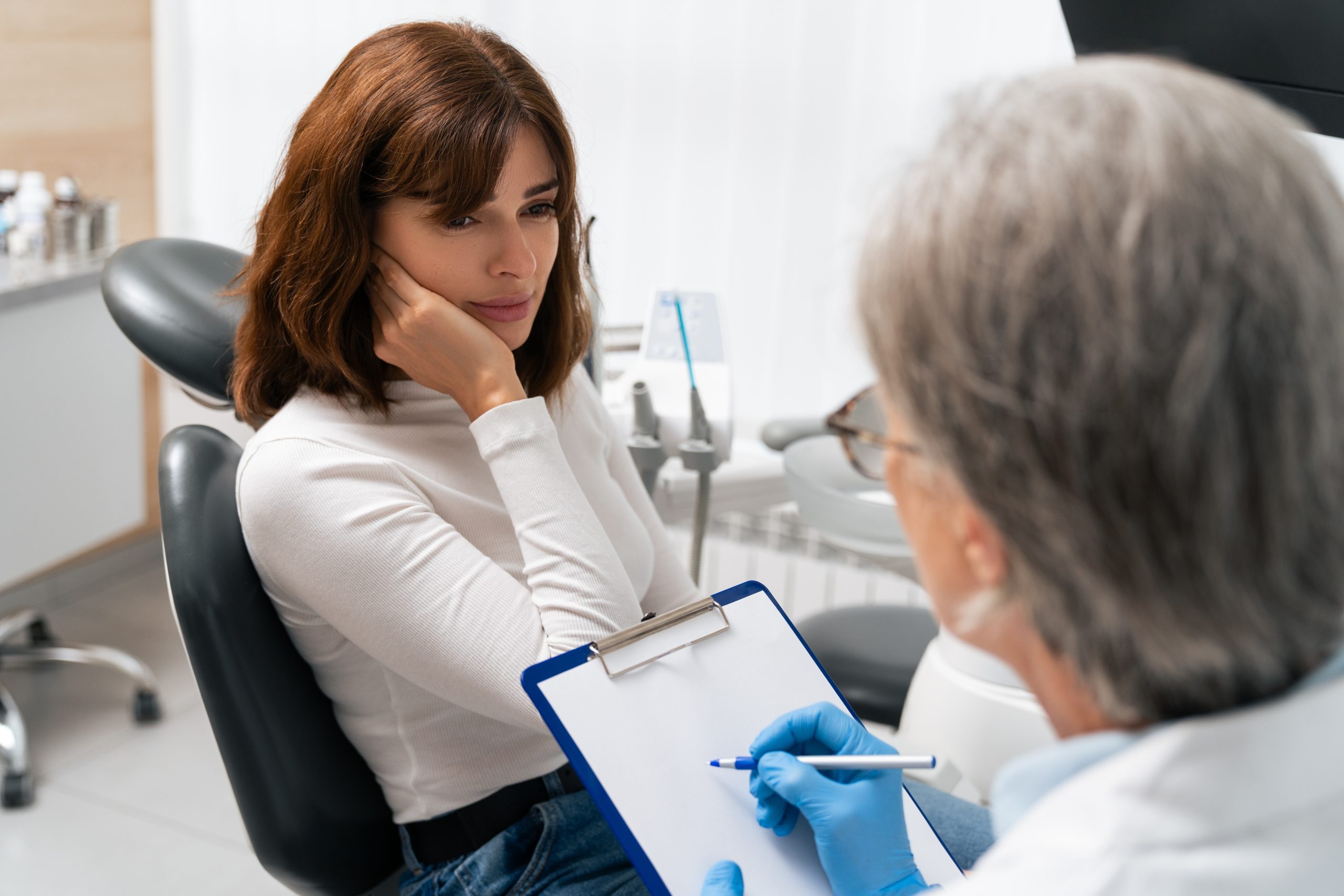 Dentist in blue gloves taking notes on clipboard while patient sits in dental chair