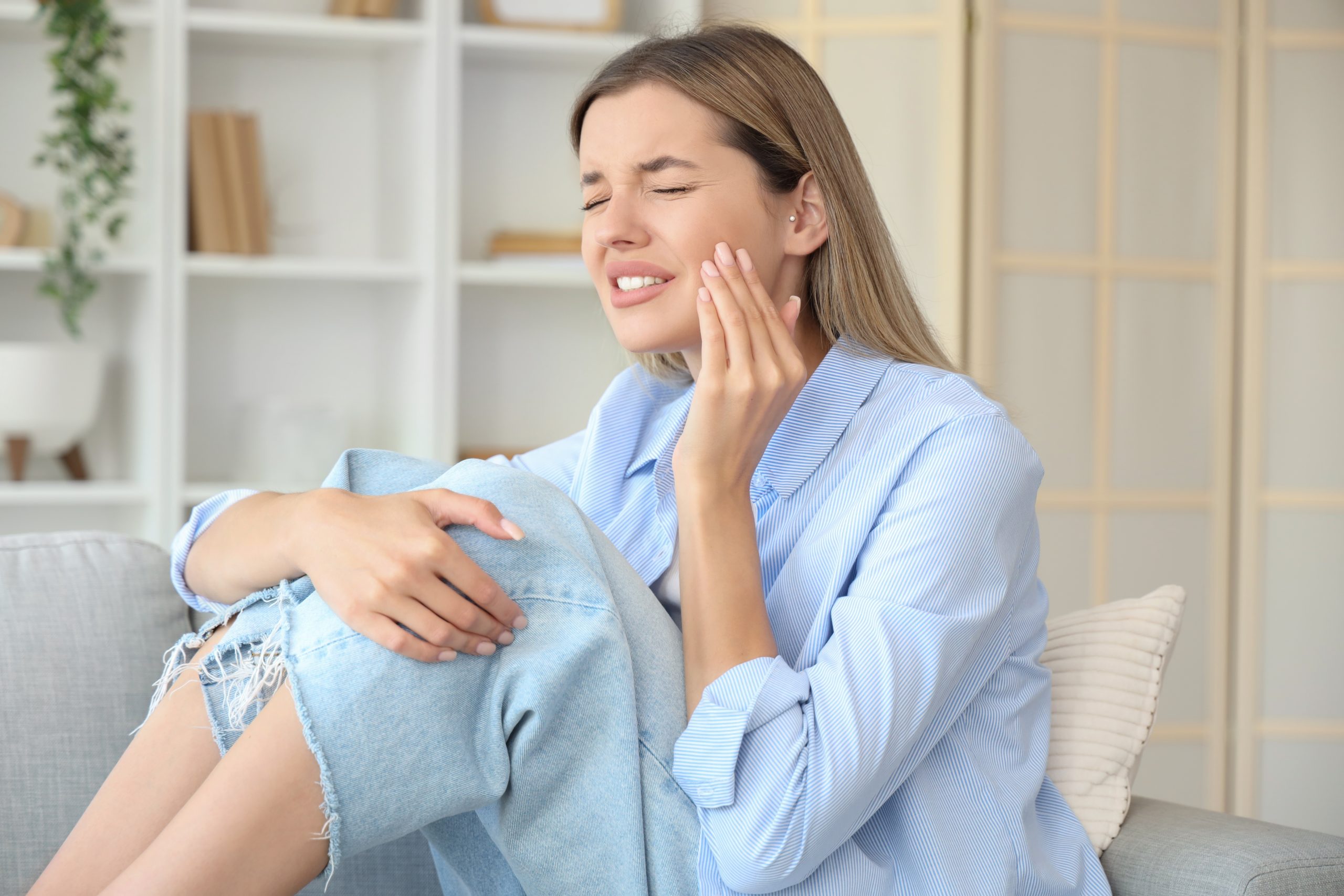 Woman holding her cheek in pain while sitting on couch